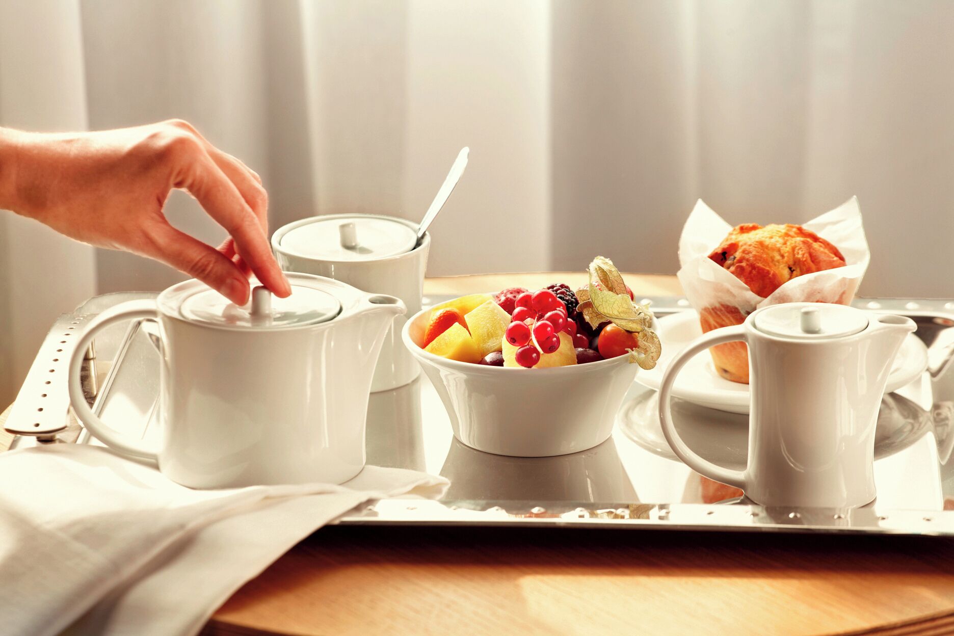 En bakke med morgenmad: en kop, en skål med frugt, en muffin og en tekedel.