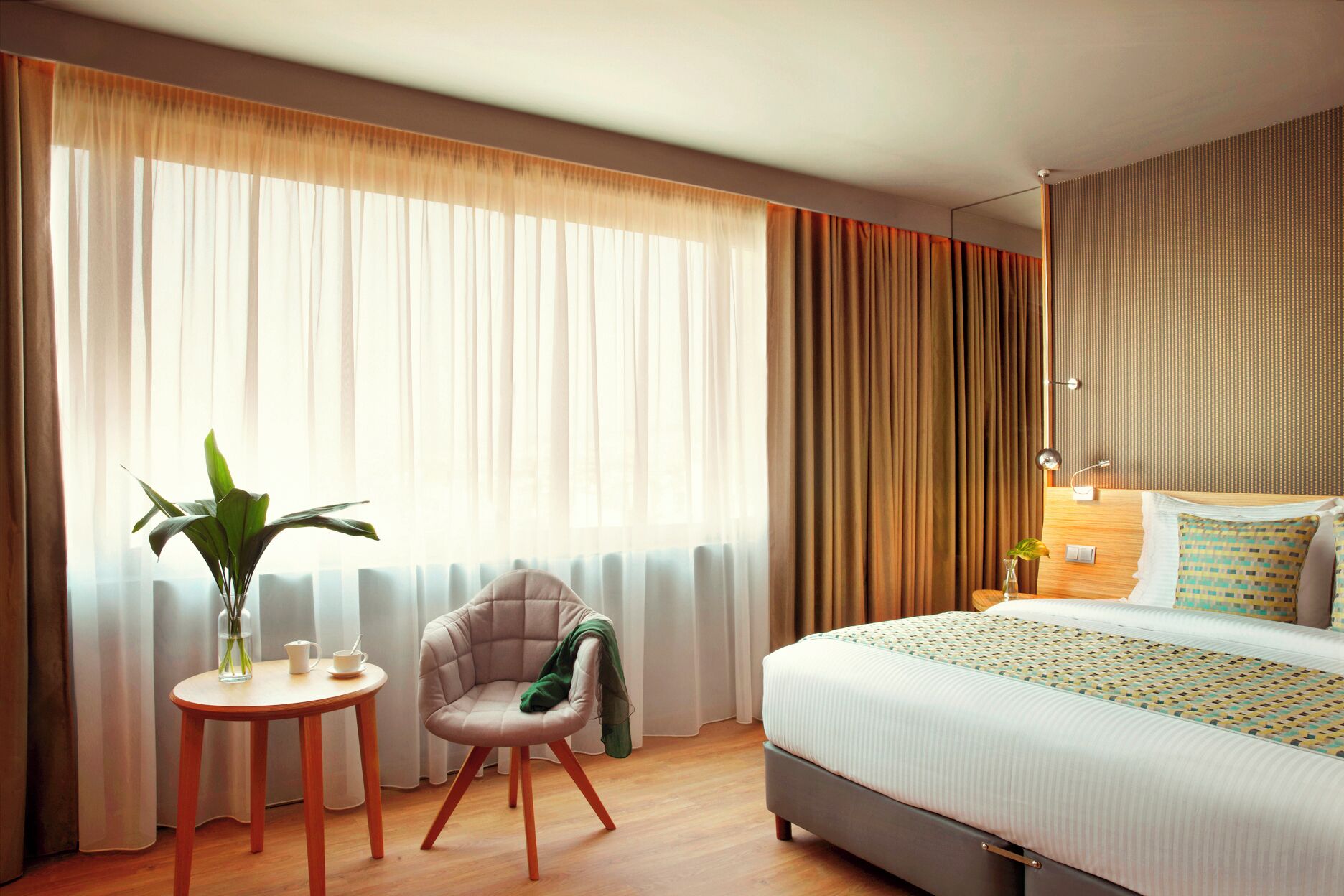 A hotel room with a bed, a chair, a small table, and a potted plant.