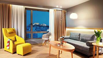 Una habitación de hotel moderna con un ventanal grande, un sofá, una silla, una mesita y una lámpara.