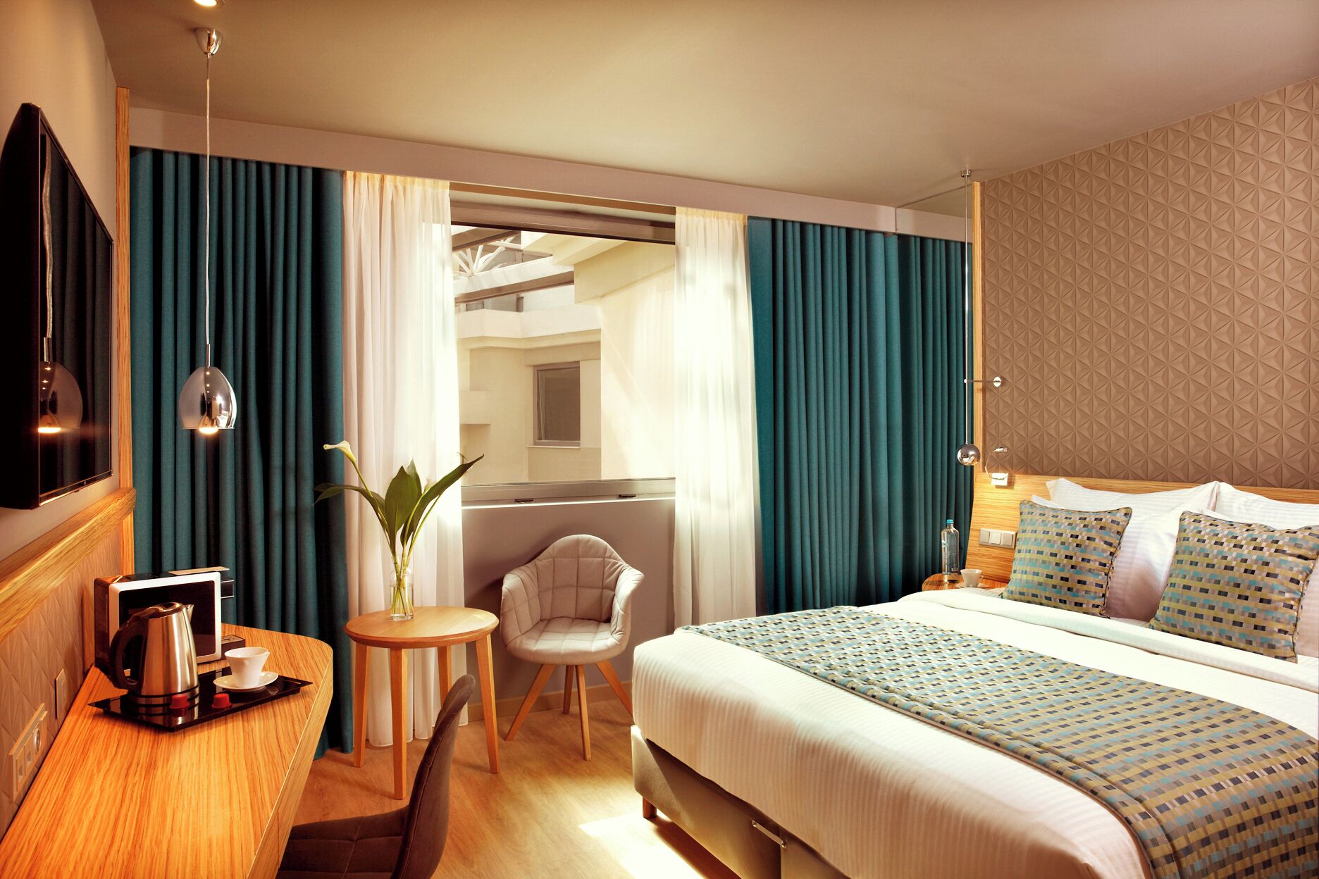 Hotellihuone, jossa on sänky, yöpöytä, lamppu, tuoli ja näkymä parvekkeelle.