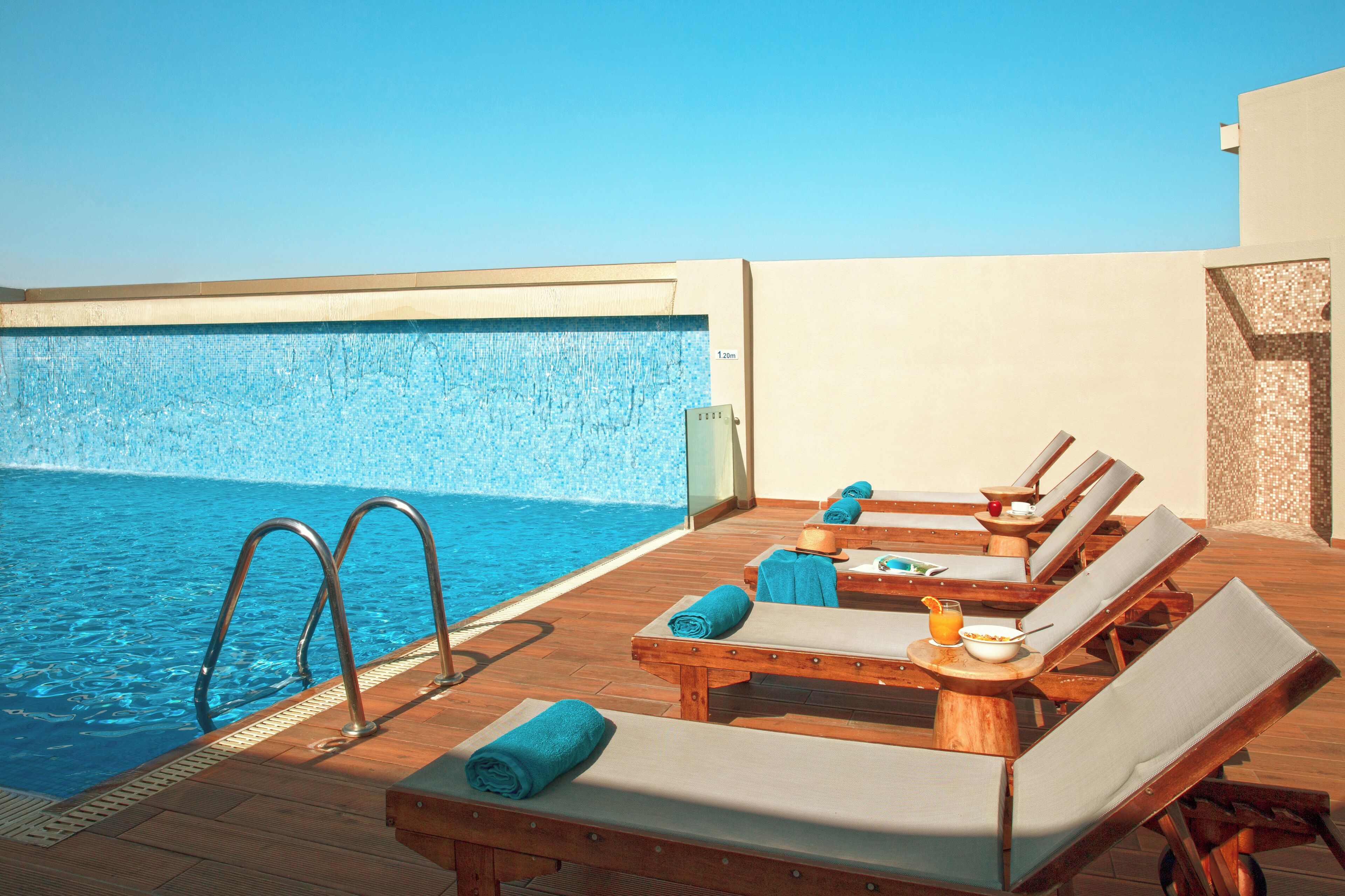 A rooftop pool area with lounge chairs, a table with breakfast items, and a clear view of the pool.