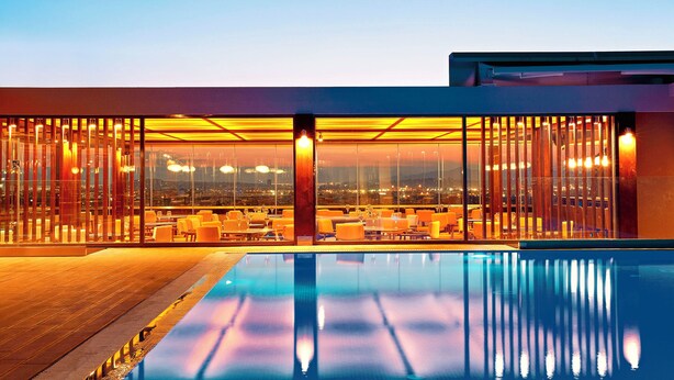 A modern hotel with a rooftop pool, glass walls, and a city view. - Zeus Wyndham Grand Athens (Athens)