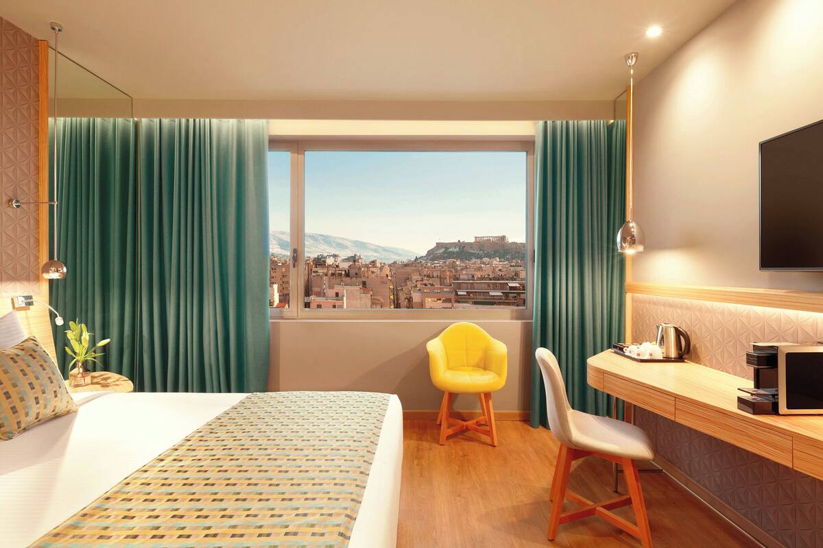 Camera d'albergo con un letto grande, una scrivania con una sedia, una TV e vista sulla città.