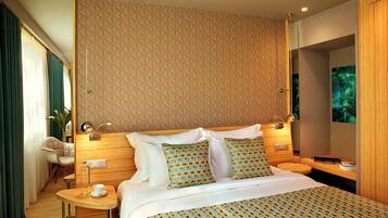 A modern hotel room with a geometric patterned headboard, a neatly made bed with patterned bedding, a small round table with a cup and a bottle, and a chair.