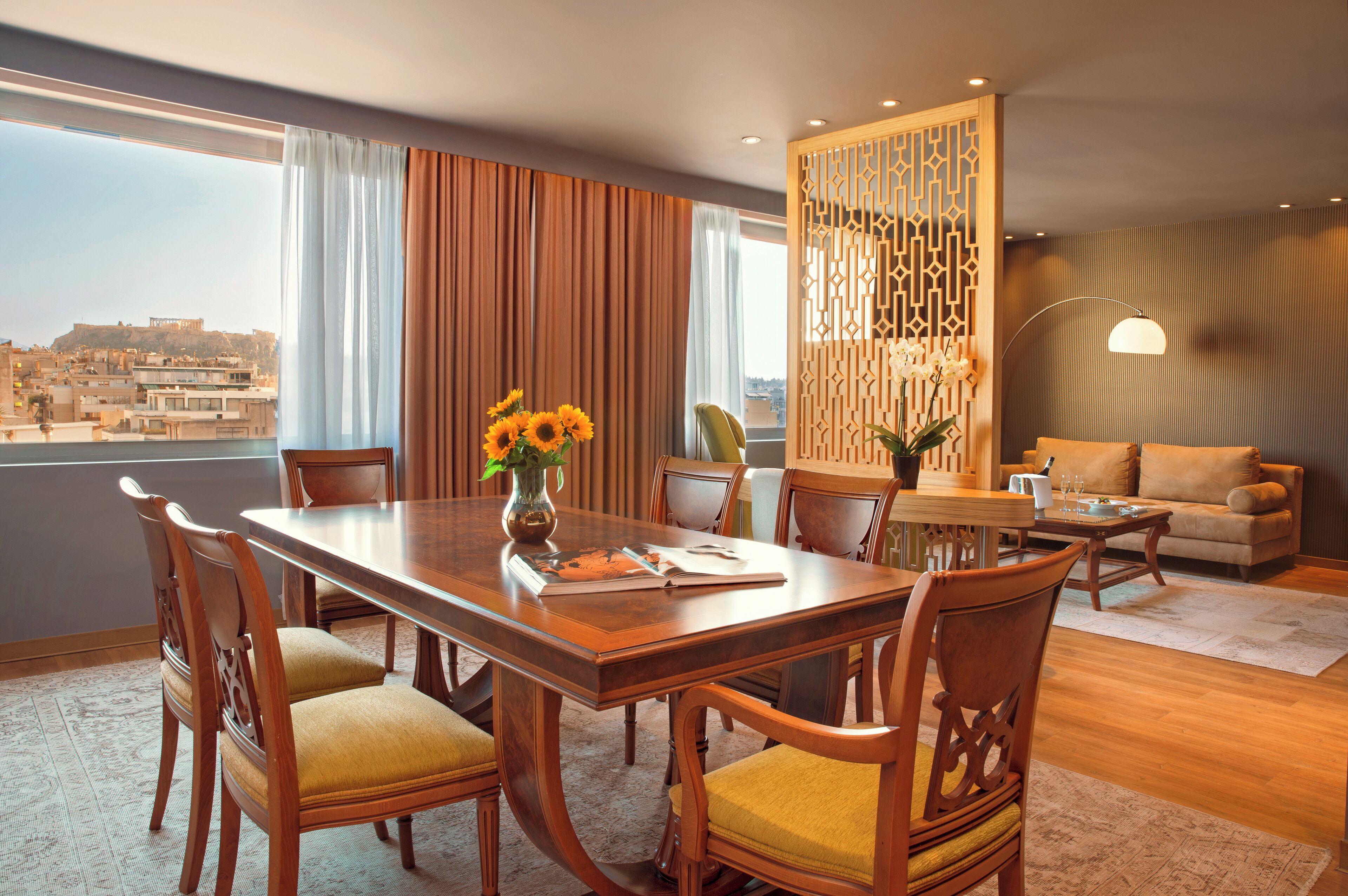 A dining area with a wooden table and chairs, a vase with flowers, and a view of the city through large windows.