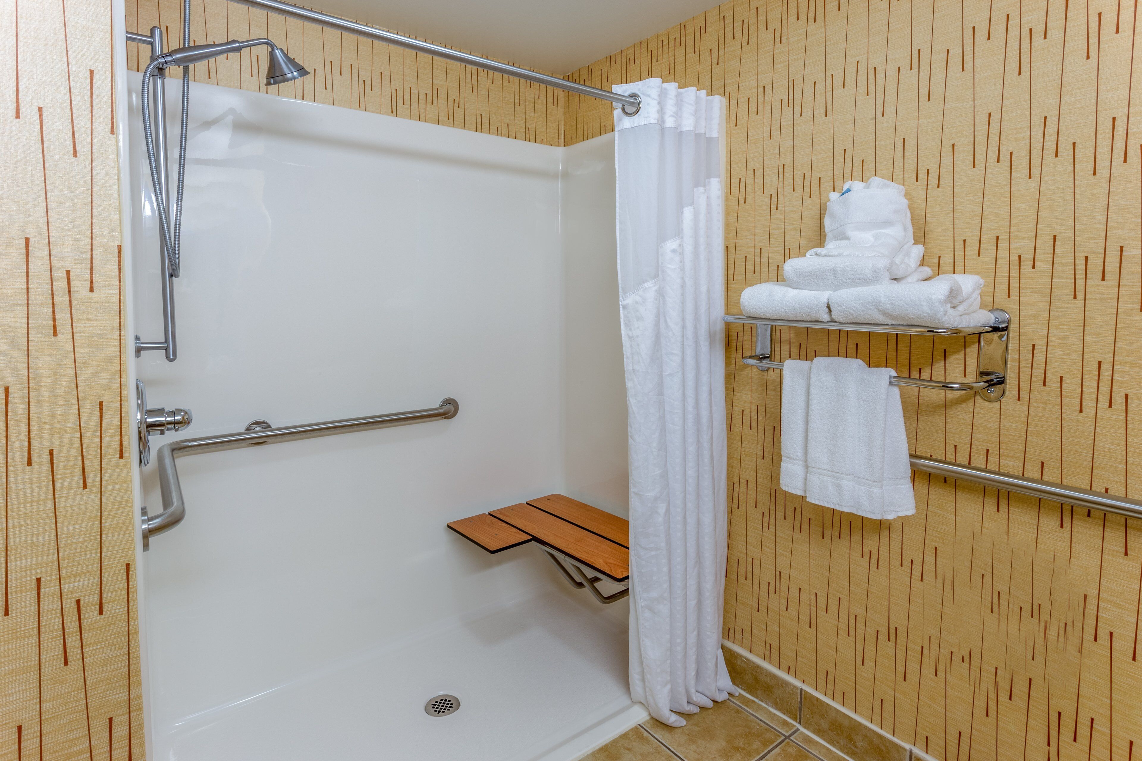 Une douche équipée d’une barre d’appui, un porte-serviettes avec des serviettes et un banc en bois.