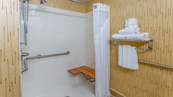 Une douche équipée d’une barre d’appui, un porte-serviettes avec des serviettes et un banc en bois.