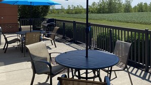 An outdoor patio with a round table and chairs, a blue umbrella, and a view of a field. - Holiday Inn Express Hotel & Suites Bowling Green by IHG (Bowling Green)