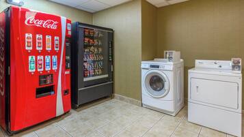 A room with a red Coca-Cola vending machine, a black refrigerator, a white washing machine, and a dryer.