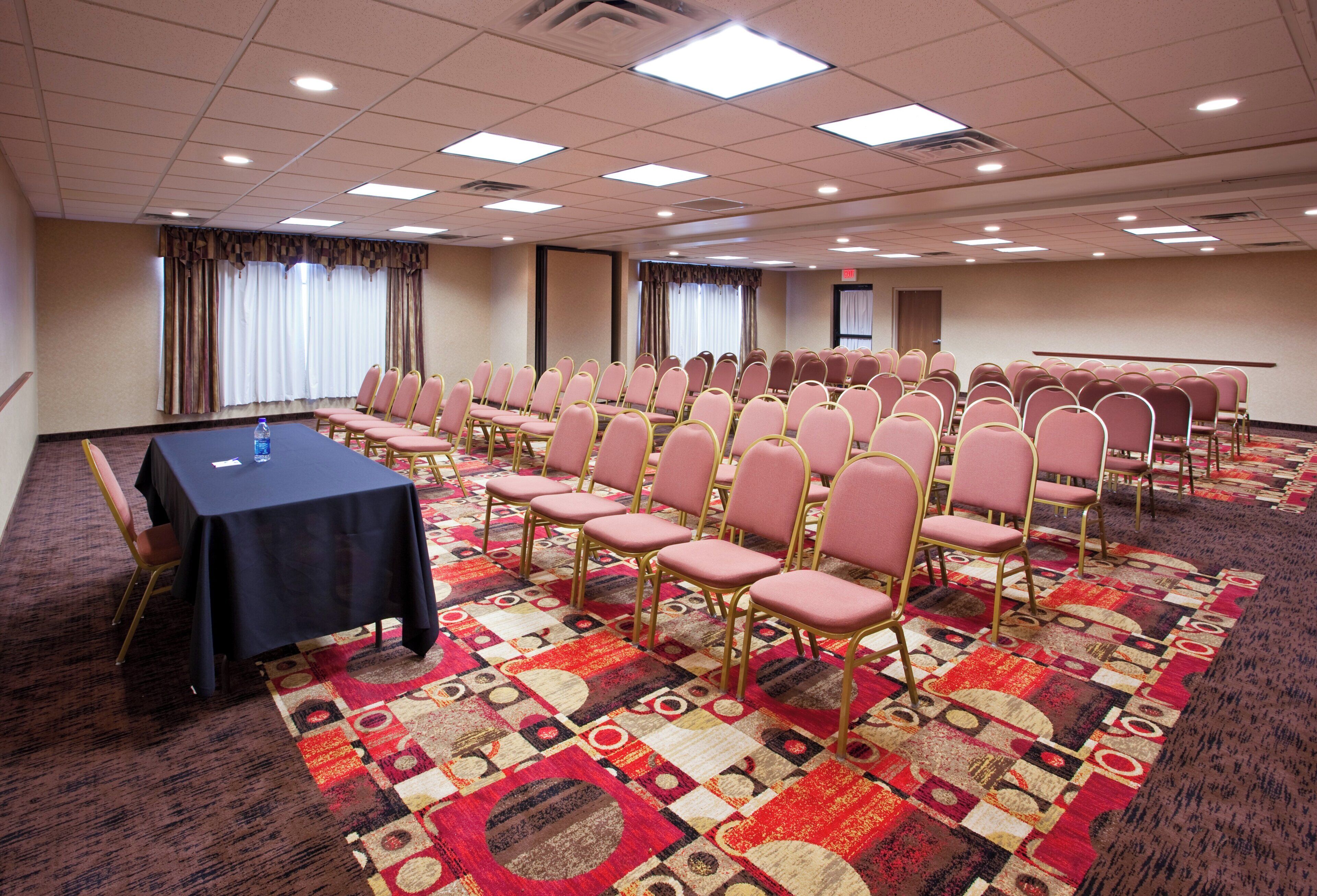 Un salón de conferencias con filas de sillas, una mesa y piso alfombrado.