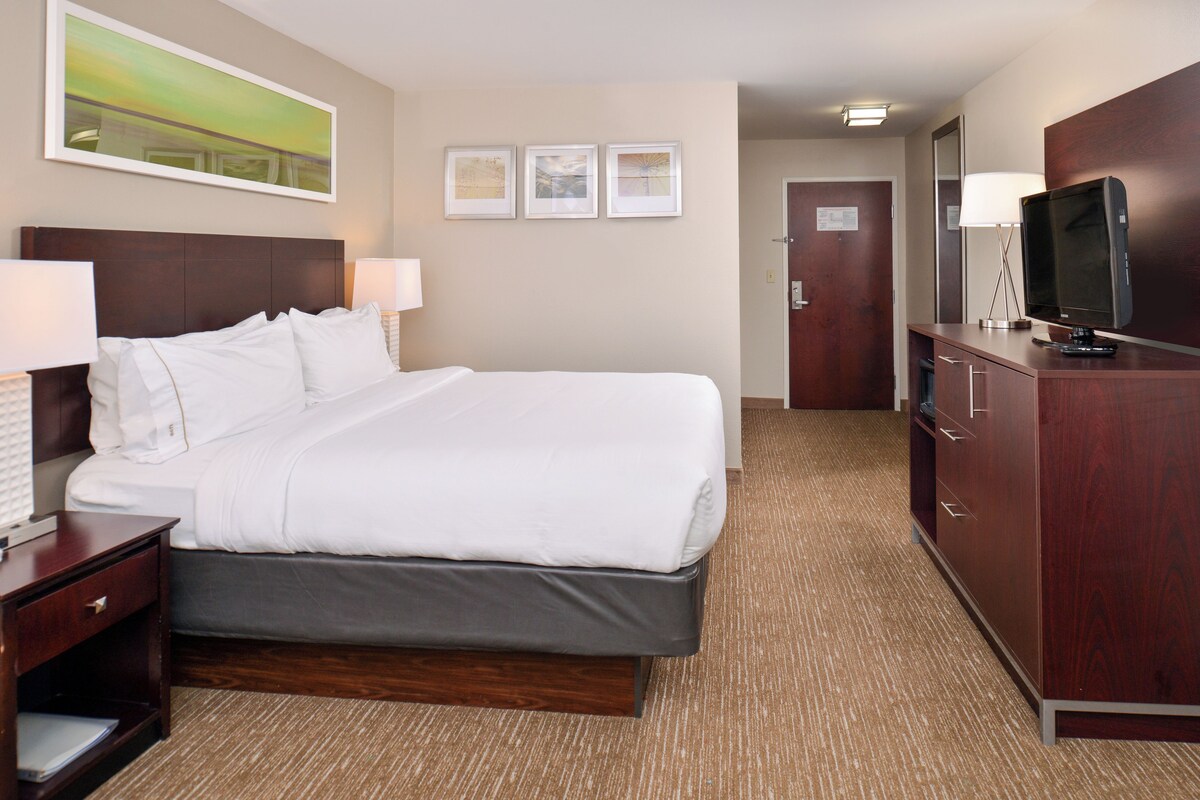 A hotel room with a bed, bedside tables, a TV, a wardrobe, and framed pictures on the wall.