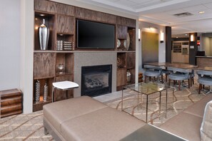 A hotel lobby with a seating area, a fireplace, a television, and a bar.