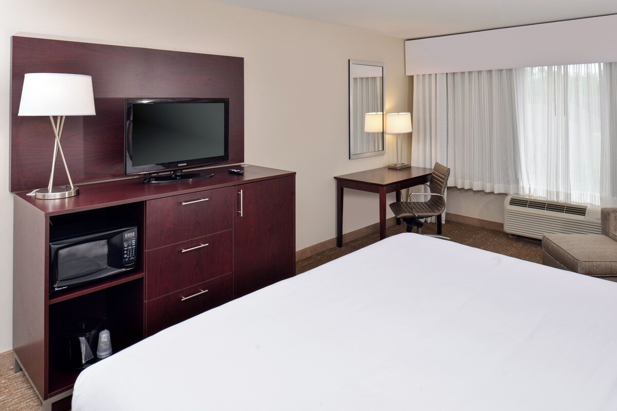 A hotel room with a bed, a TV, a desk with a chair, a microwave, and a lamp.