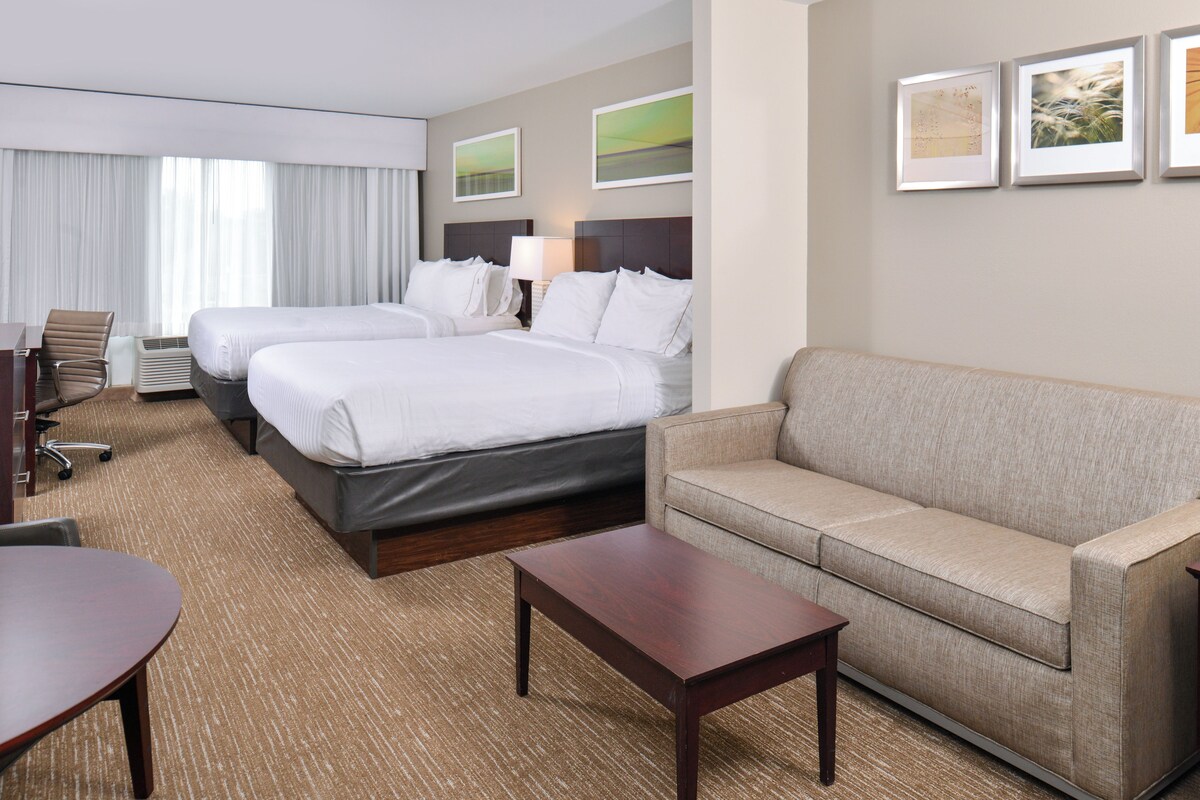 A hotel room with two beds, a sofa, a desk, and a chair.