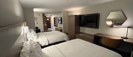 A hotel room with two beds, a desk, a TV, and a mirror.