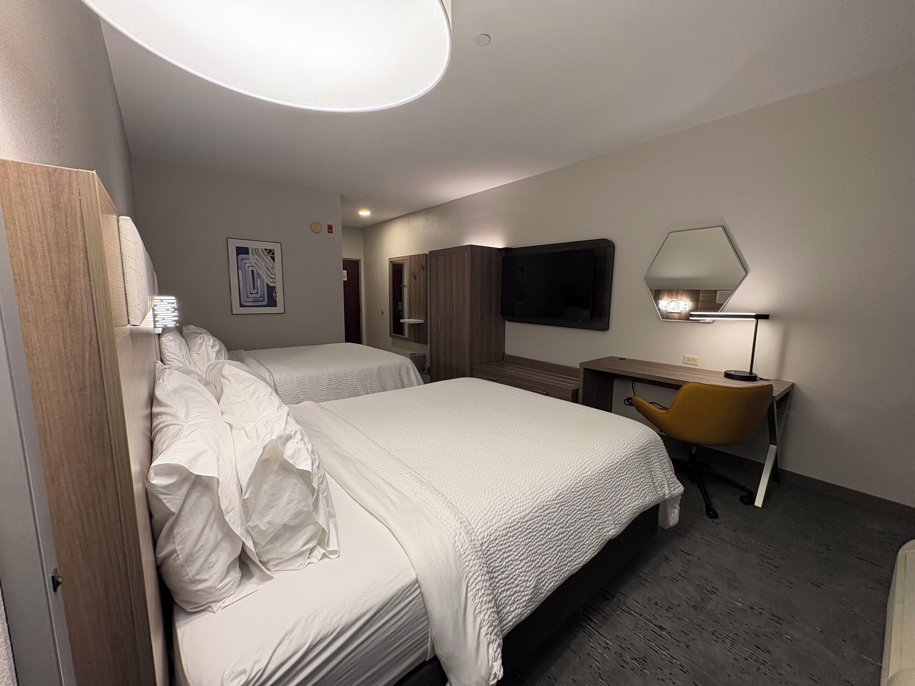 Ett hotellrum med två sängar, ett skrivbord, en stol, en TV och en lampa.