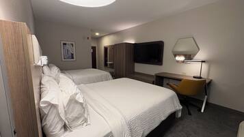 Ett hotellrum med två sängar, ett skrivbord, en stol, en TV och en lampa.