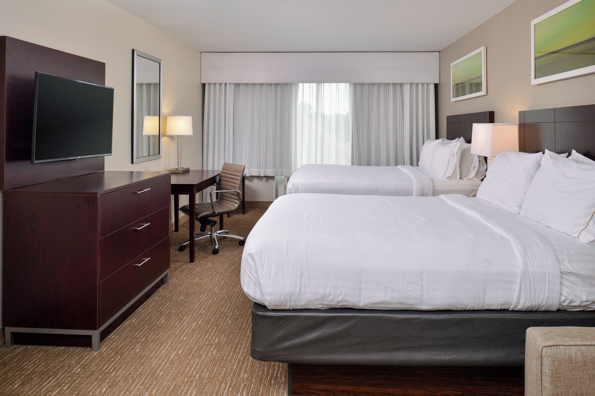 A hotel room with a large bed, a desk with a chair, a television, and a dresser.