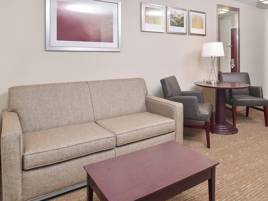 A hotel room with a beige sofa, two armchairs, a small wooden table, and a lamp.