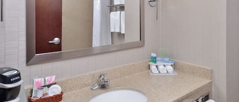 A hotel bathroom with a sink, mirror, towel rack, and a coffee machine.