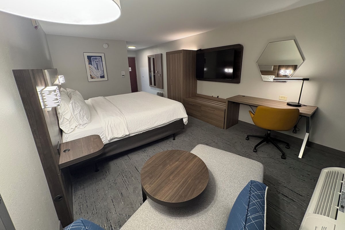 A hotel room with a bed, a desk, a chair, a round table, a TV, and a mirror.
