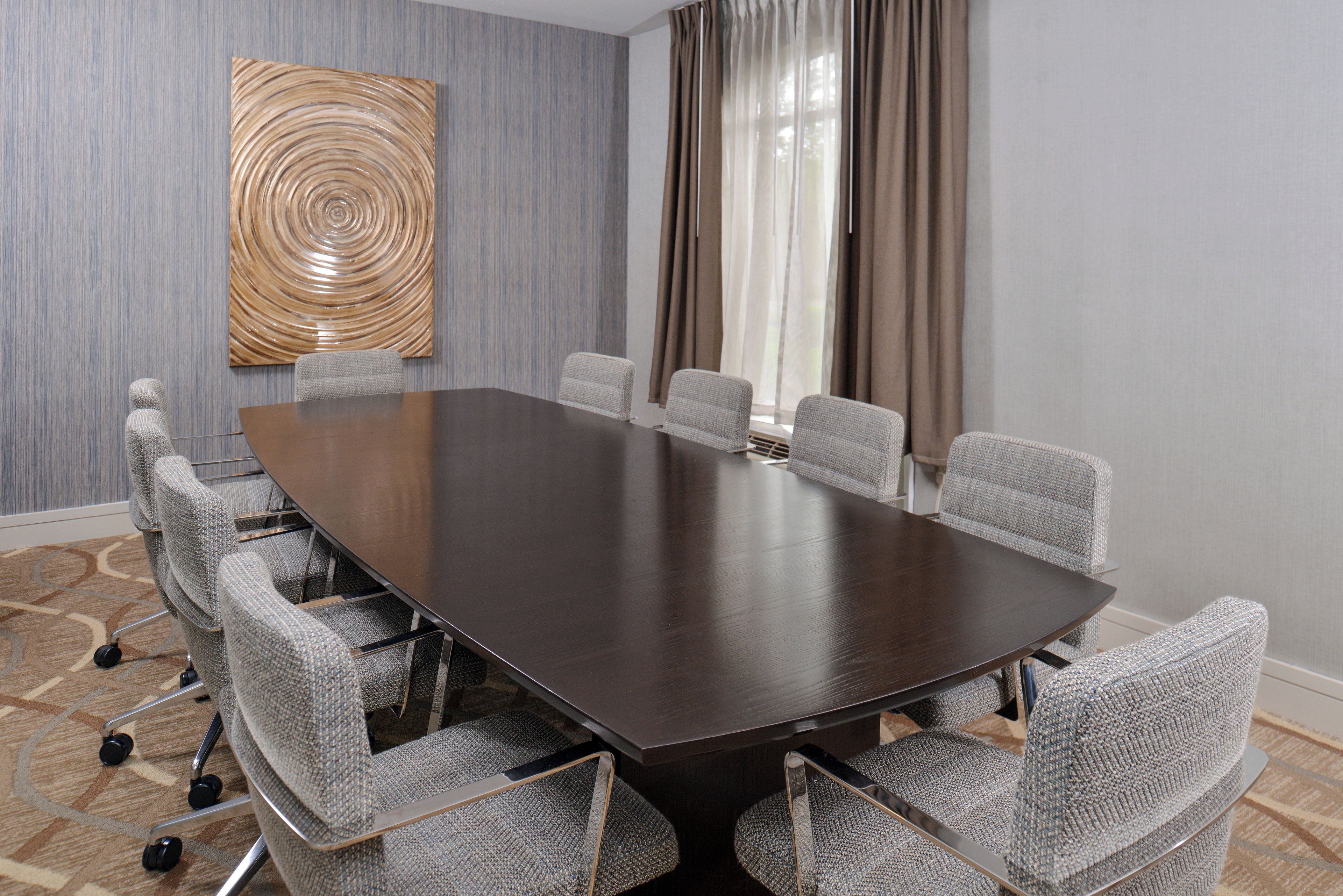 A conference room with a dark wooden table and six grey upholstered chairs with wheels.