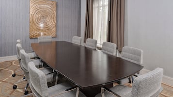 A conference room with a dark wooden table and six grey upholstered chairs with wheels.