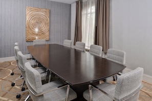 Un salón de conferencias con una mesa de madera oscura y seis sillas grises tapizadas con ruedas.