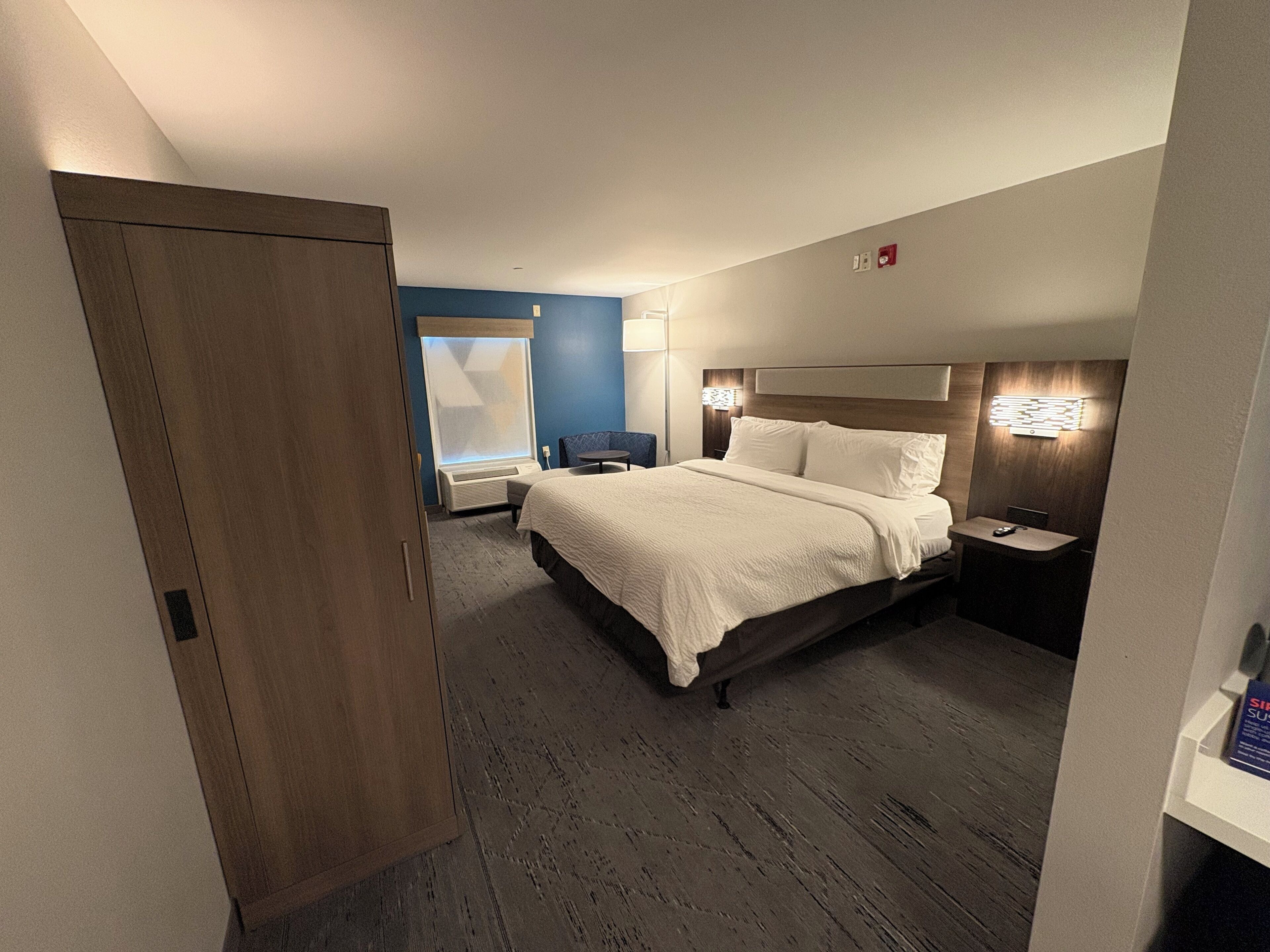 Quarto de hotel com uma cama grande, mesas de cabeceira, escrivaninha e uma cadeira.