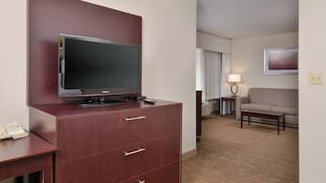 Ein Hotelzimmer mit Fernseher am Flachbildschirm auf einer Holzkommode, einem Sofa, einem kleinen Tisch und einer Lampe.