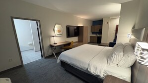 Quarto de hotel moderno com cama grande, escrivaninha, cadeira, televisão e cozinha compacta.
