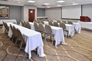 A conference room with rows of tables and chairs, a projector screen, and a carpeted floor. - Holiday Inn Express Hotel & Suites Lafayette by IHG (Lafayette)