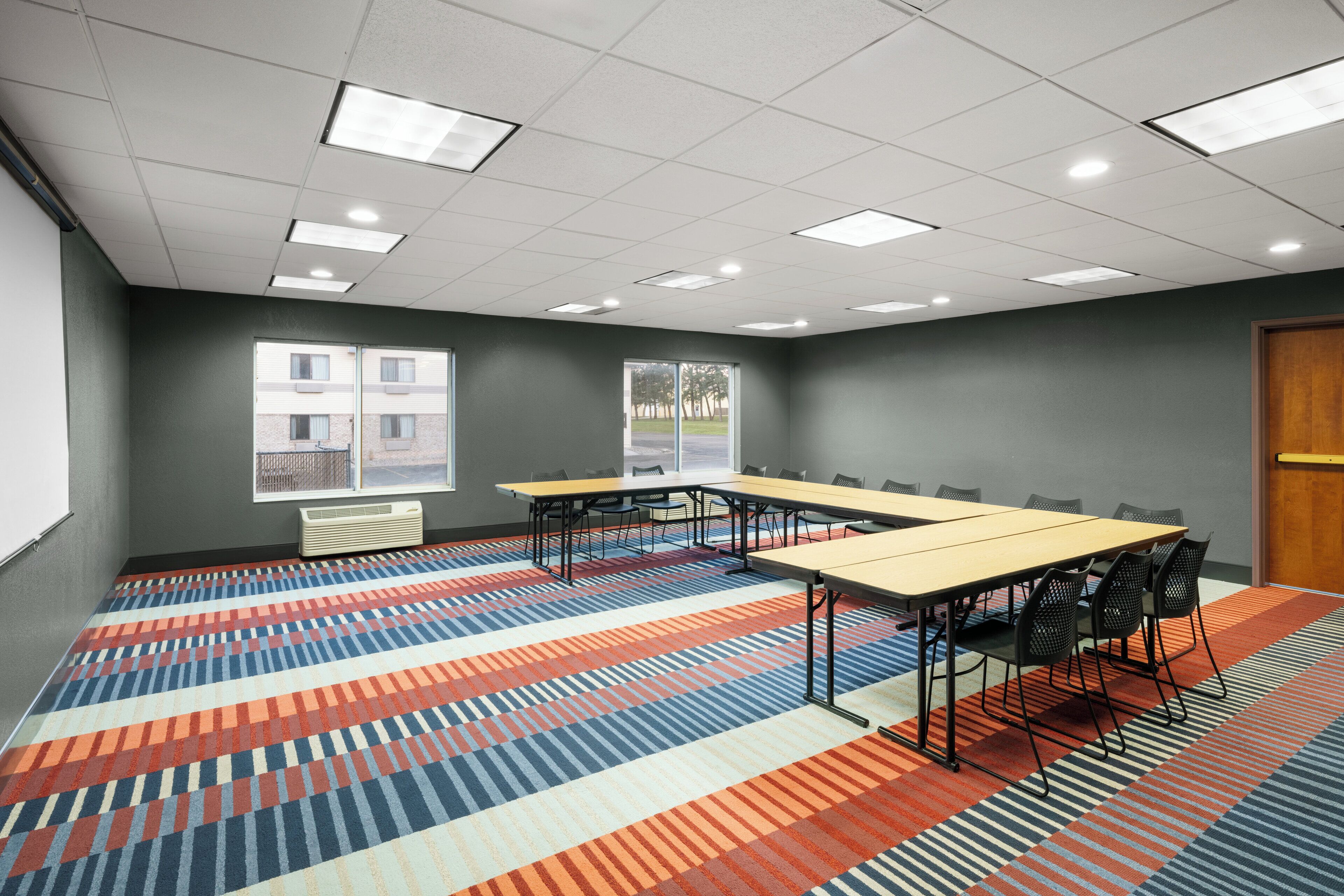 A conference room with a large table, chairs, a projector screen, and a patterned carpet.