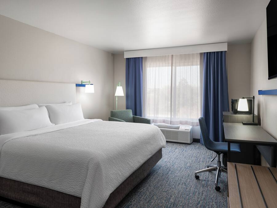 A hotel room with a large bed, a desk, a chair, a TV, and a window with curtains.