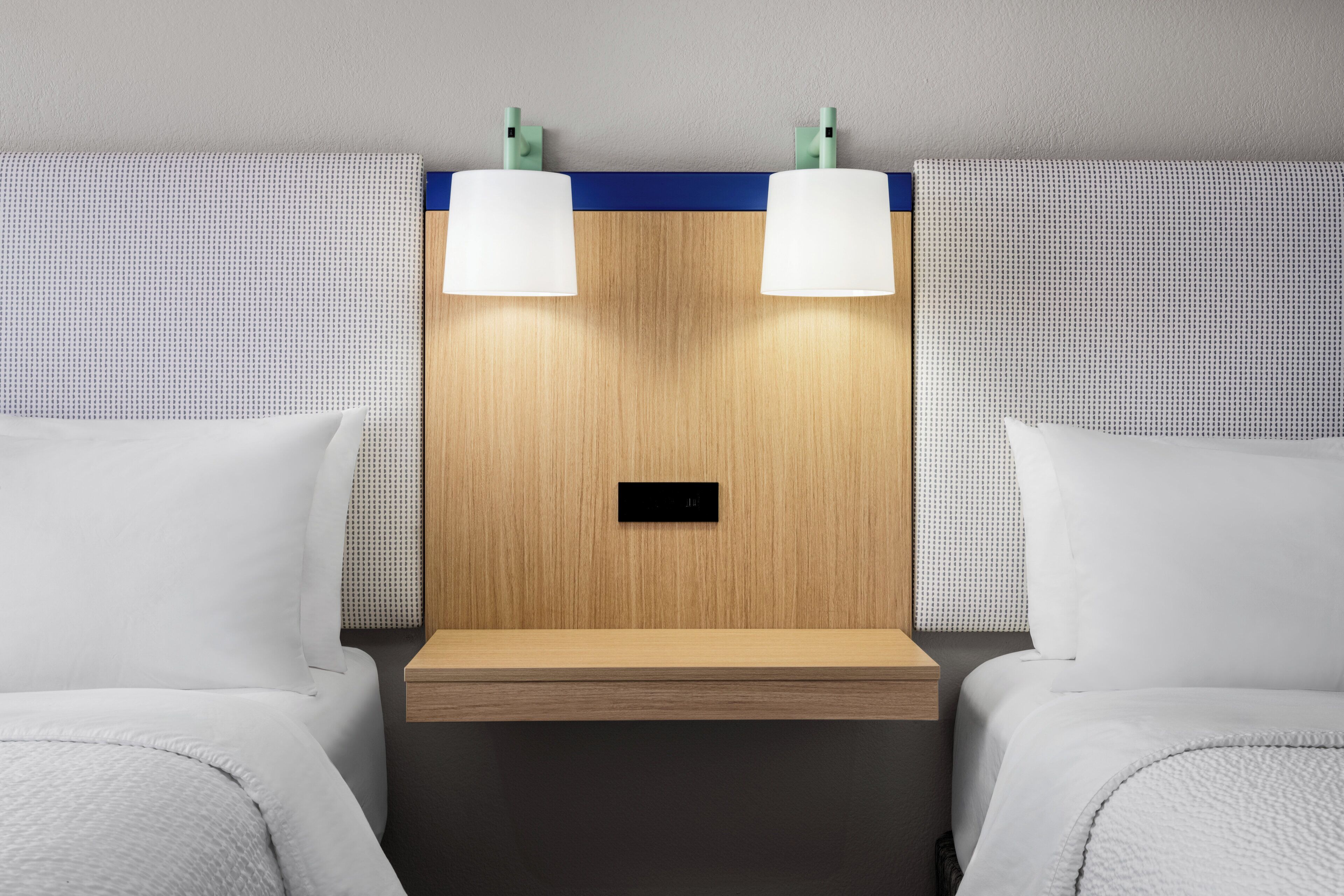 Une chambre d’hôtel avec deux lits, une tête de lit en bois et deux lampes fixées au mur.