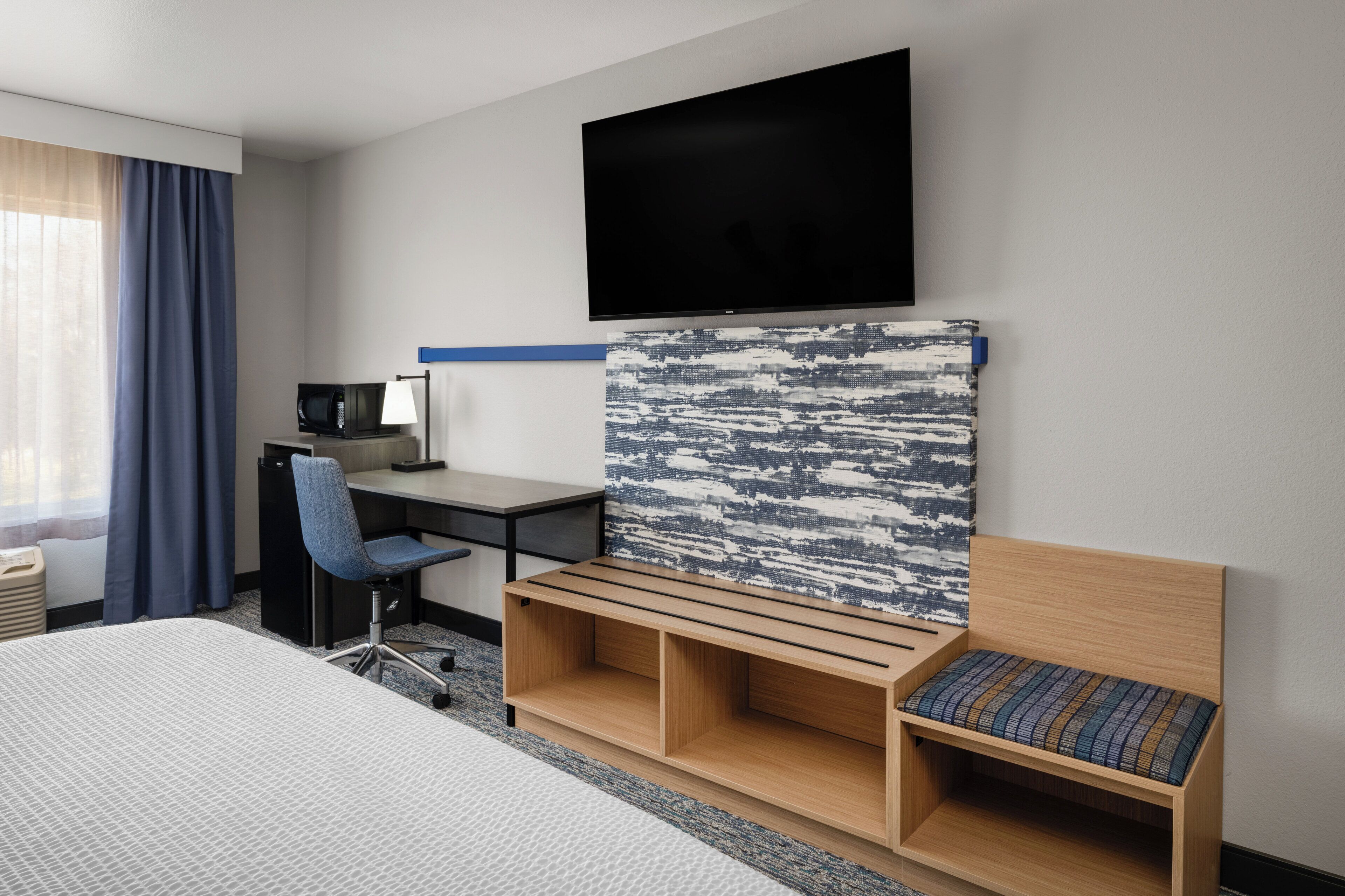 Habitación de hotel con cama, escritorio, silla, televisión y una obra de arte colgada en la pared.