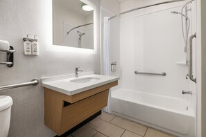 Et moderne badeværelse med en hvid vask, et trækommode, en glasbrusekabine og et gelænder.
