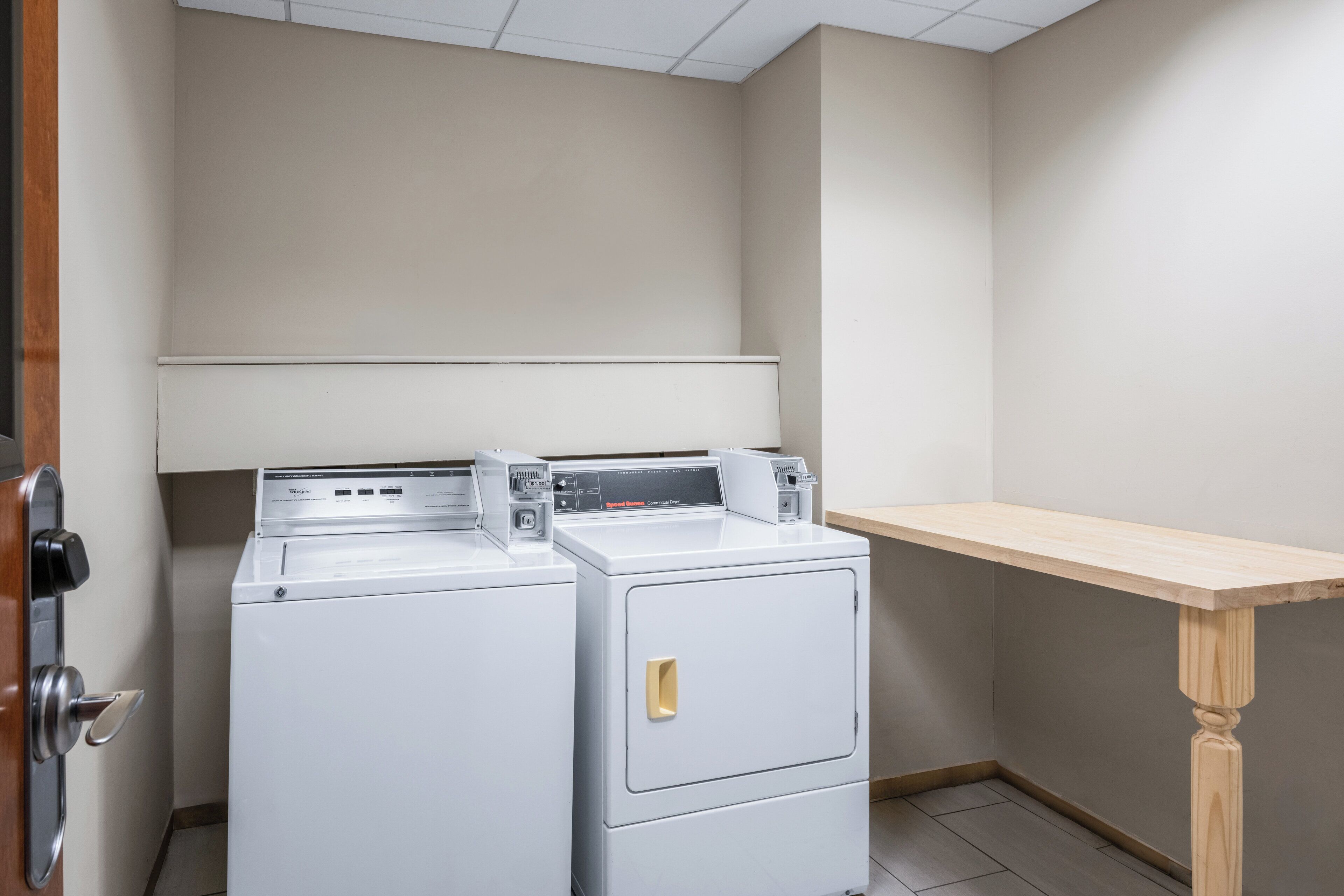 A laundry area with two stacked washers and dryers, a wooden table, and a door with a handle.
