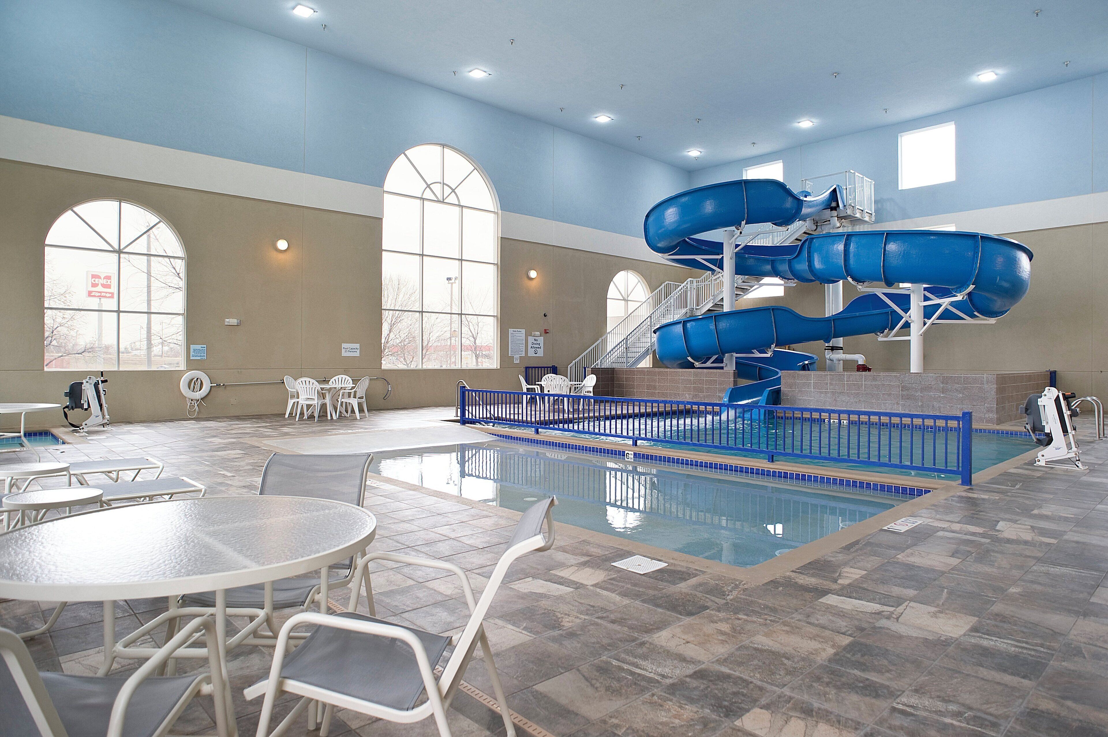 An indoor swimming pool with multiple slides, seating areas, and a clear view of the sky through large windows.