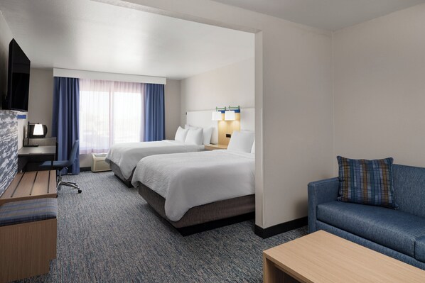 Een hotelkamer met twee bedden, een bureau, een televisie, een bank en een raam met gordijnen.