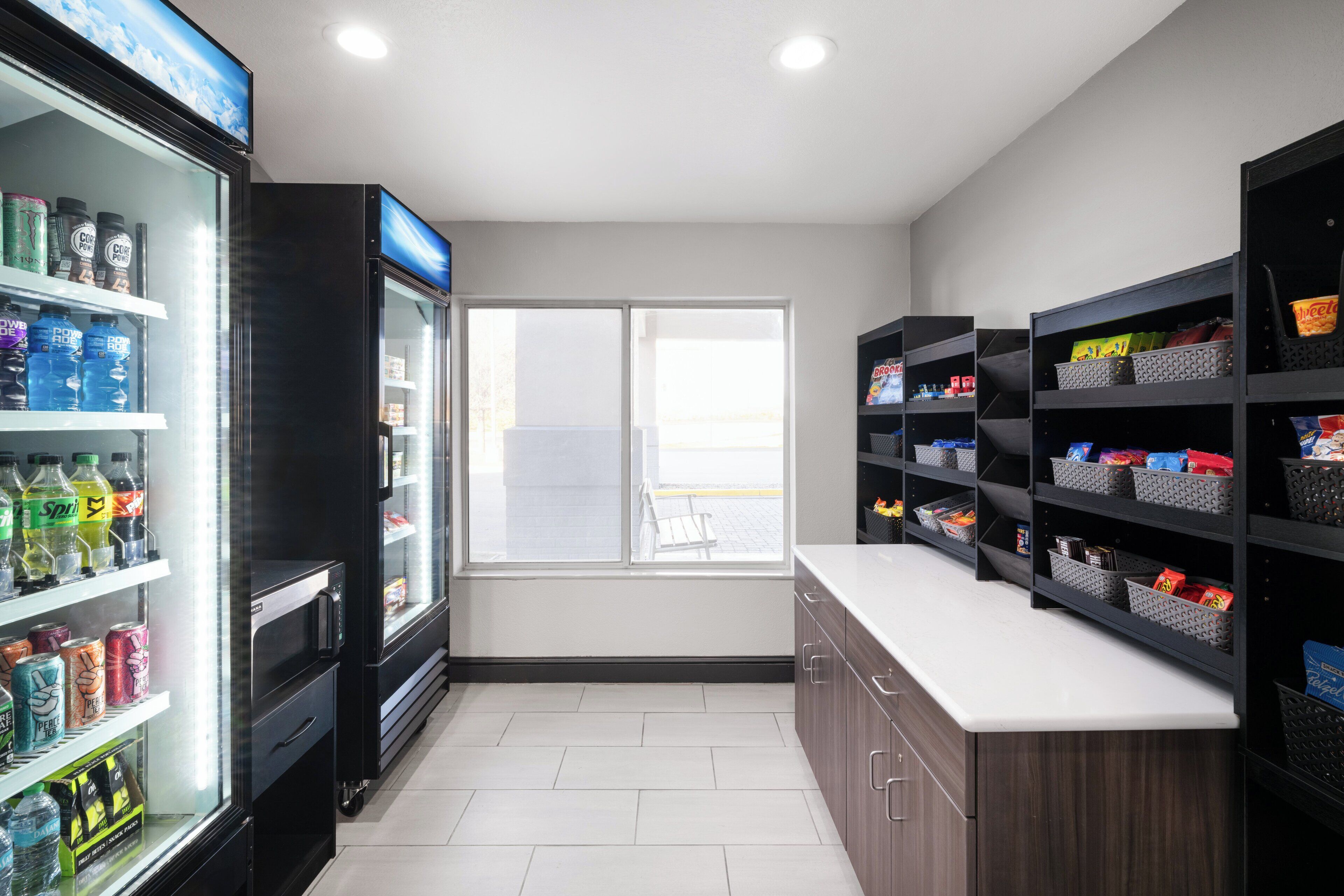 A clean, modern kitchenette with a refrigerator stocked with beverages, a microwave, and a sink.