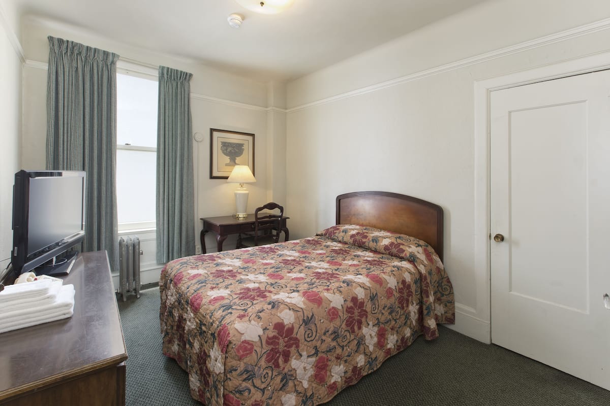 Une chambre d’hôtel avec un lit, un bureau avec une lampe, une télévision et une porte.