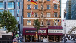 Un edificio a più piani con una scala antincendio, bandiere e vetrine che includono Boost Mobile, Rainbow Pizza e ADA Hotel.