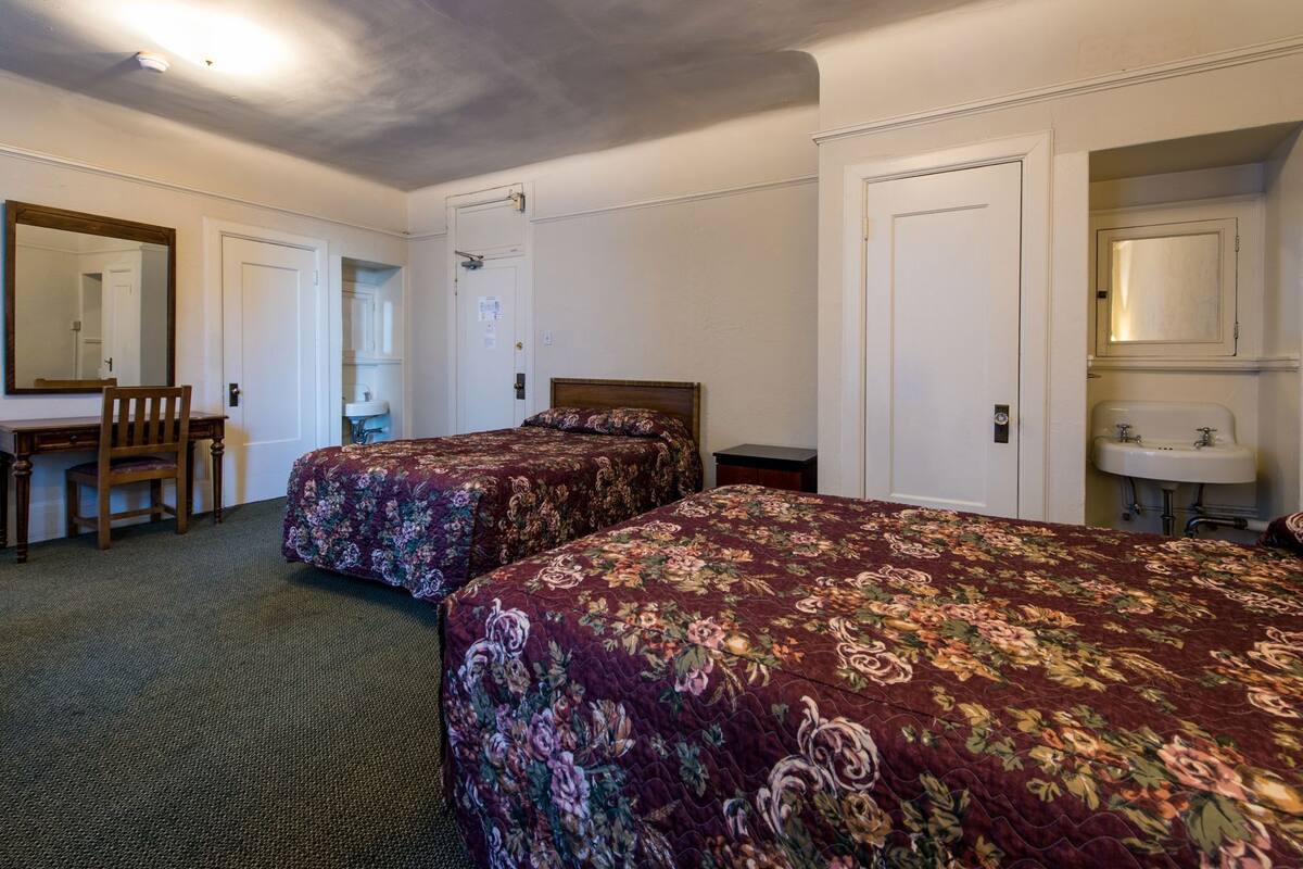 Une chambre d’hôtel avec deux lits, un bureau, une chaise, un miroir, une porte et un lavabo.