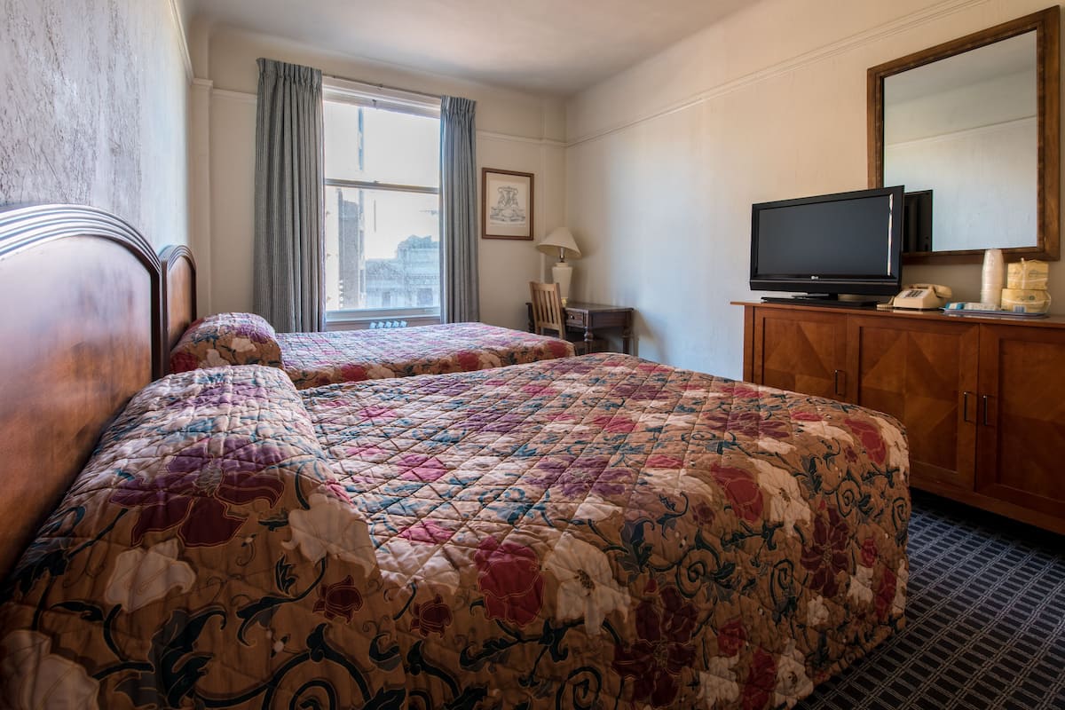 Une chambre d’hôtel avec deux lits, une télévision, un bureau avec une lampe et une fenêtre avec des rideaux.