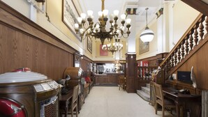 Una hall d'albergo con un juke-box d'epoca, pannelli in legno, un grande lampadario e una scala.
