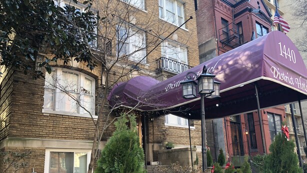 A brick building with a 'Distillery Hotel' sign, outdoor seating area with purple umbrellas, and potted plants. - District Hotel (Washington)