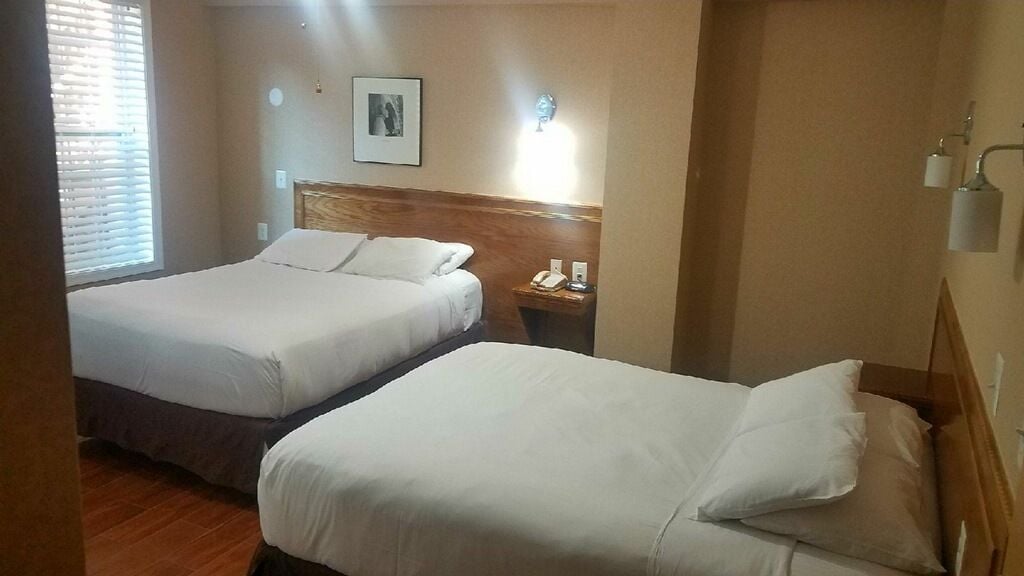 Habitació d'hotel amb dos llits, un panell de capçalera de fusta, una taula de nit amb un telèfon i una làmpada fixada a la paret.