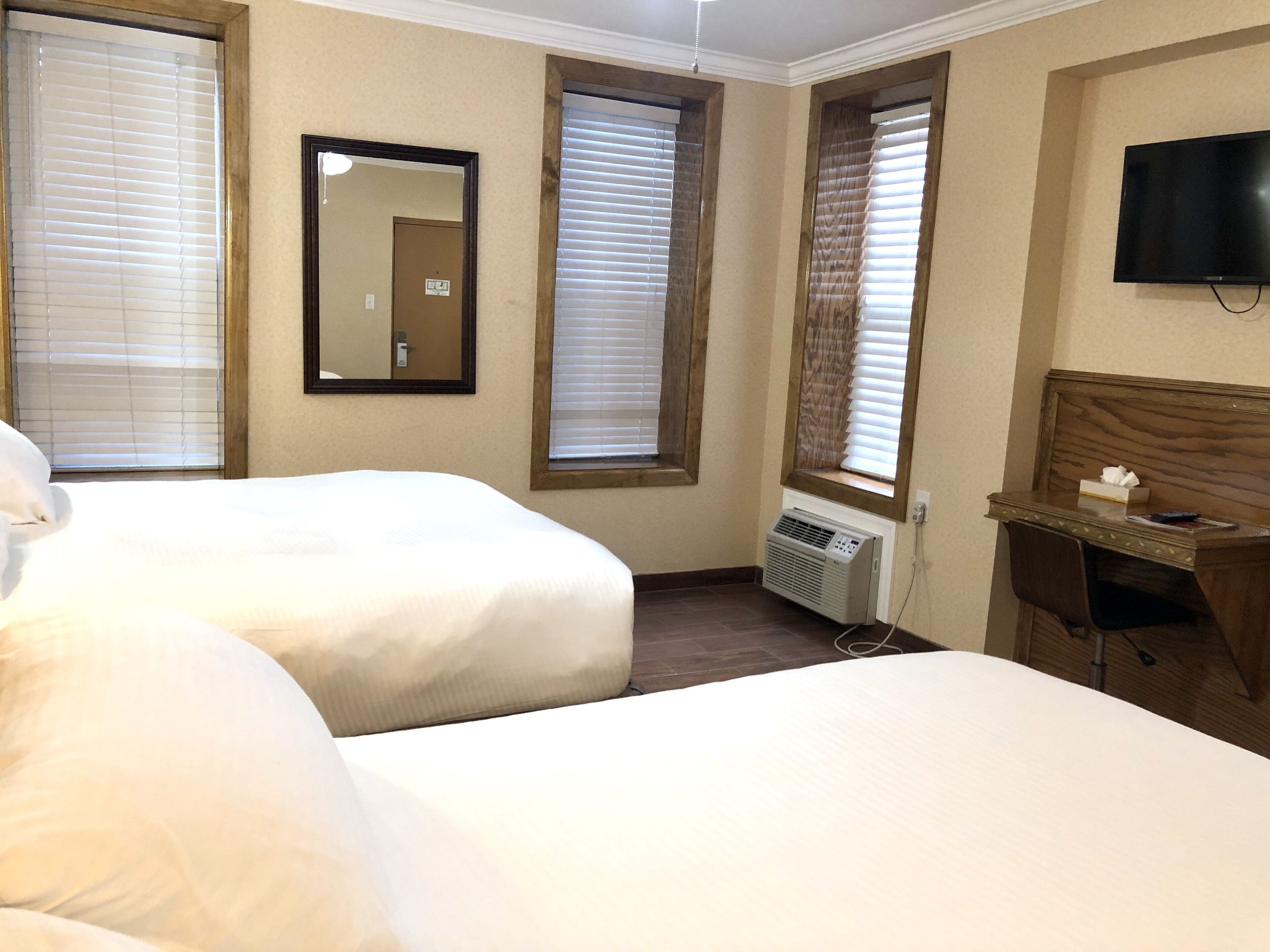 Habitación de hotel con dos camas, un escritorio, un televisor y una ventana con persianas.