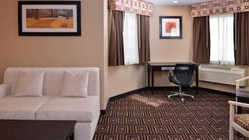 A hotel room with a sofa, a desk, a chair, and a patterned carpet.